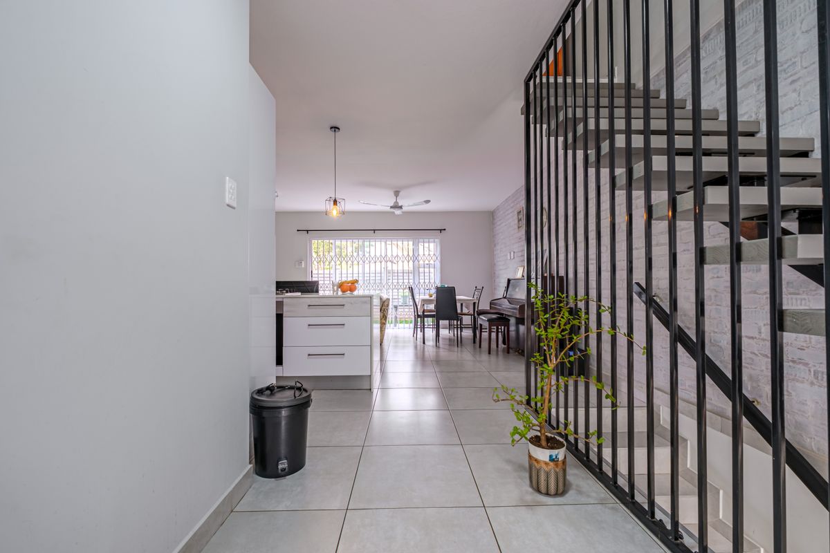 Open-plan living and kitchen area featuring modern tiled flooring, a striking metal staircase balustrade, and direct access to the outdoor space.
