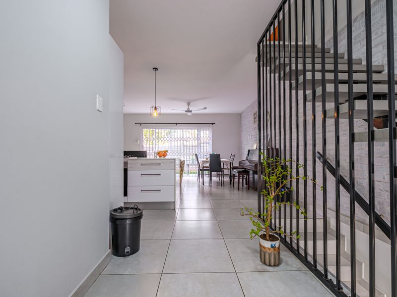 Open-plan living and kitchen area featuring modern tiled flooring, a striking metal staircase balustrade, and direct access to the outdoor space.