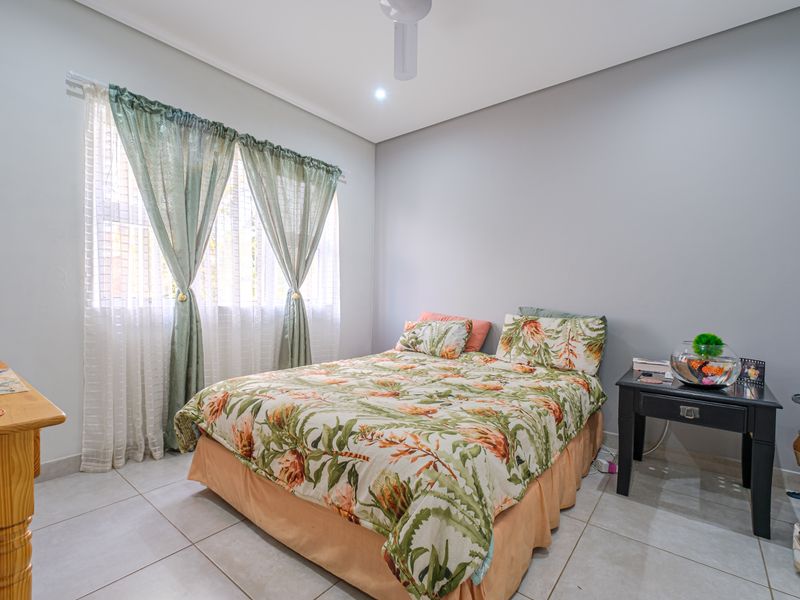 A well-lit bedroom featuring neutral wall tones, tiled flooring, and a ceiling fan, offering a comfortable and functional living space.