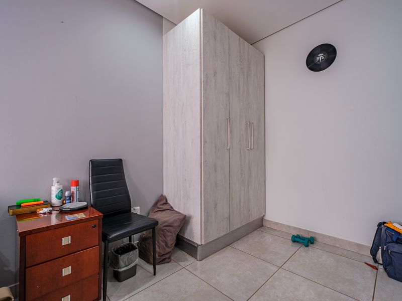 A bedroom featuring light wood-grain built-in wardrobes and neutral tiled flooring, offering a clean and functional space.