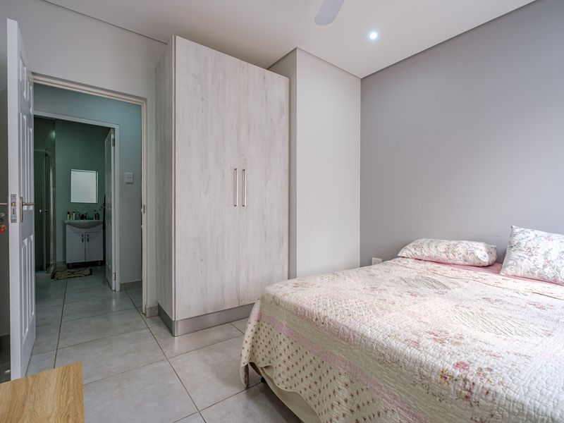 A well-maintained bedroom featuring neutral wall tones, tiled flooring, a built-in wardrobe, and direct access to an en-suite bathroom.