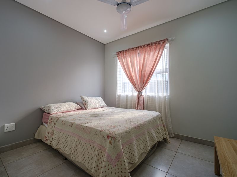 A well-maintained bedroom featuring neutral grey walls, tiled flooring, a ceiling fan, and a built-in cupboard.