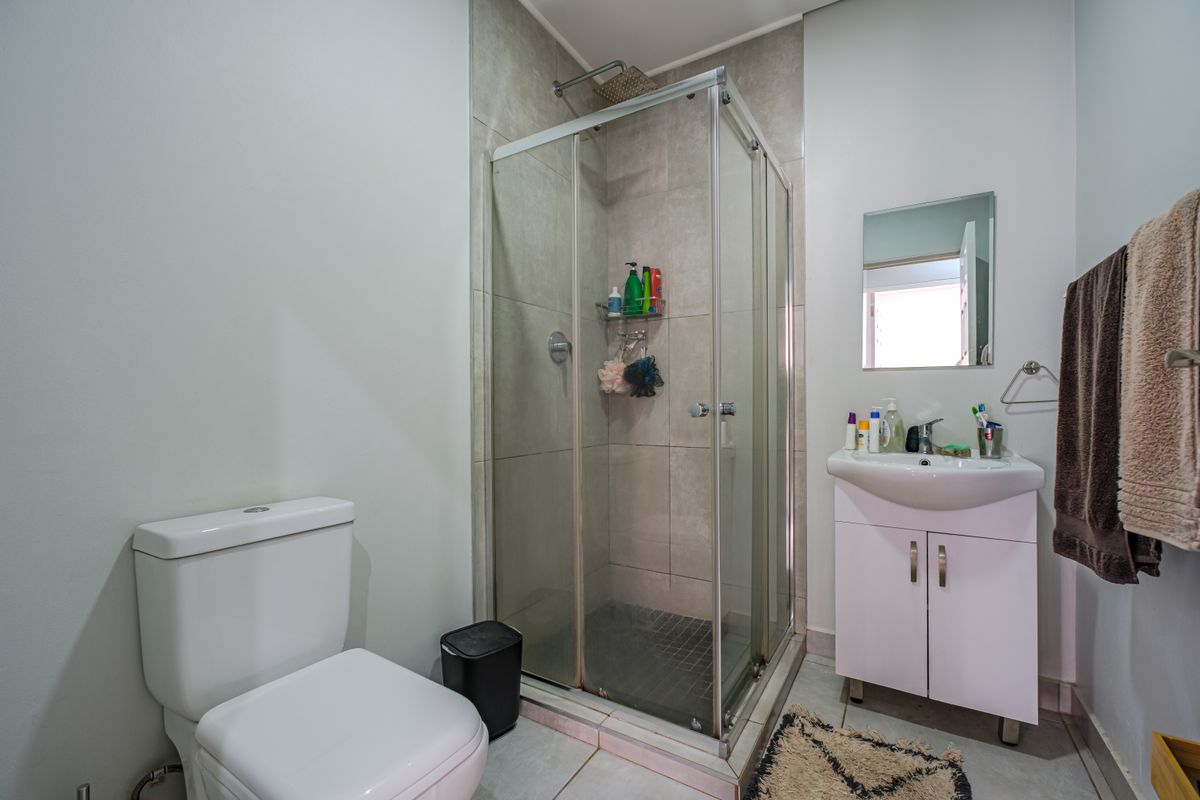 A functional bathroom featuring a corner shower enclosure, a white vanity unit with integrated basin, and a standard toilet.
