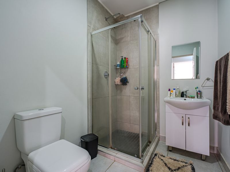 A functional bathroom featuring a corner shower enclosure, a white vanity unit with integrated basin, and a standard toilet.