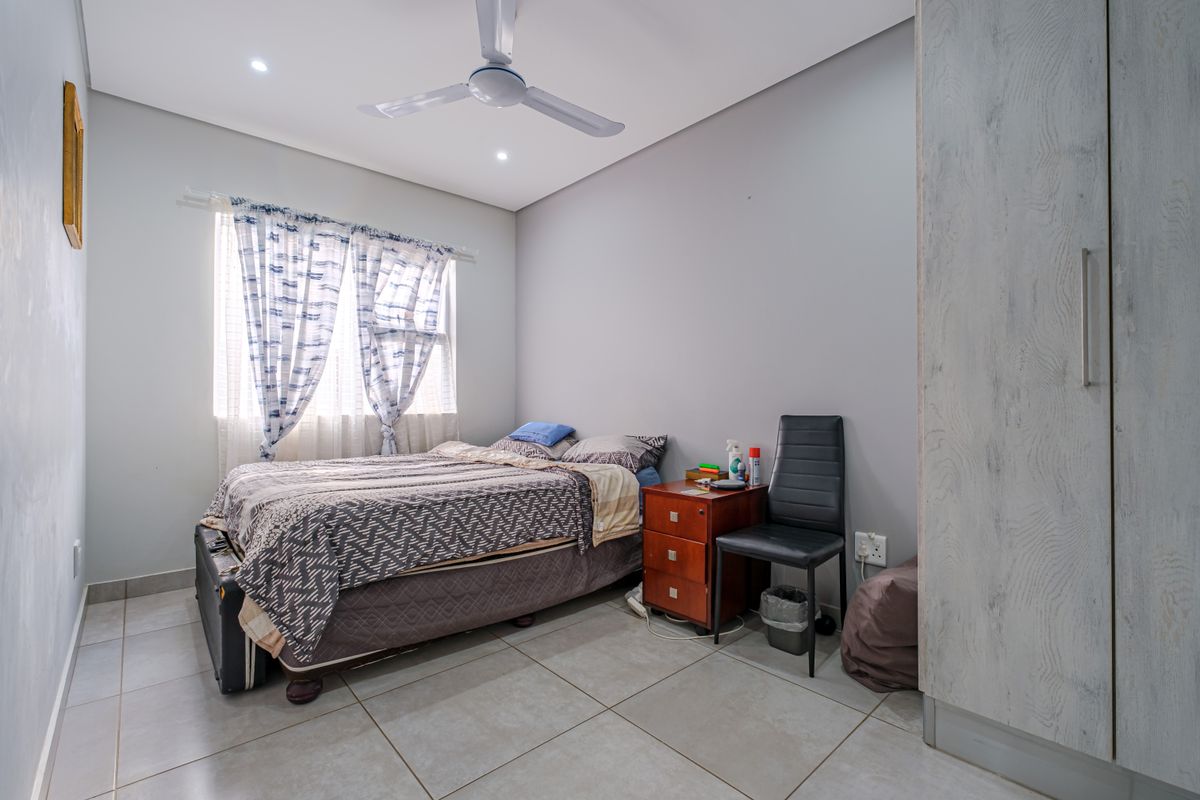 A well-maintained bedroom featuring neutral tiled flooring, built-in cupboards, and a ceiling fan, providing a clean and functional living space.