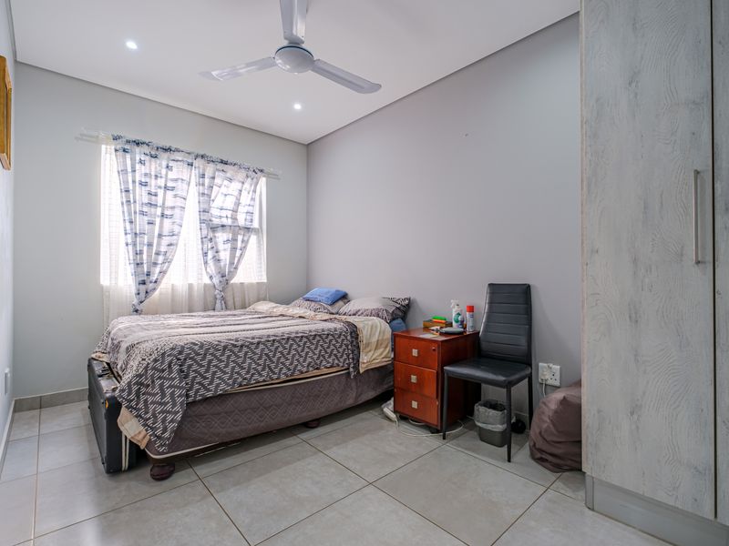 A well-maintained bedroom featuring neutral tiled flooring, built-in cupboards, and a ceiling fan, providing a clean and functional living space.
