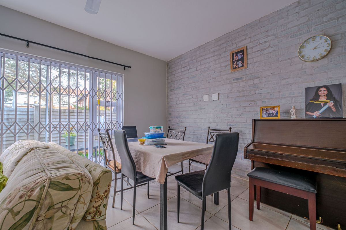 Living and dining area featuring an exposed brick wall, tiled flooring, and a sliding glass door with security gate leading to the exterior.