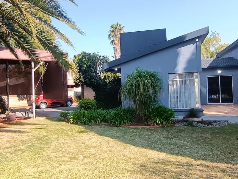 Rear view of the property featuring a modern architectural design, a covered carport, a paved walkway, and a well-maintained garden area.