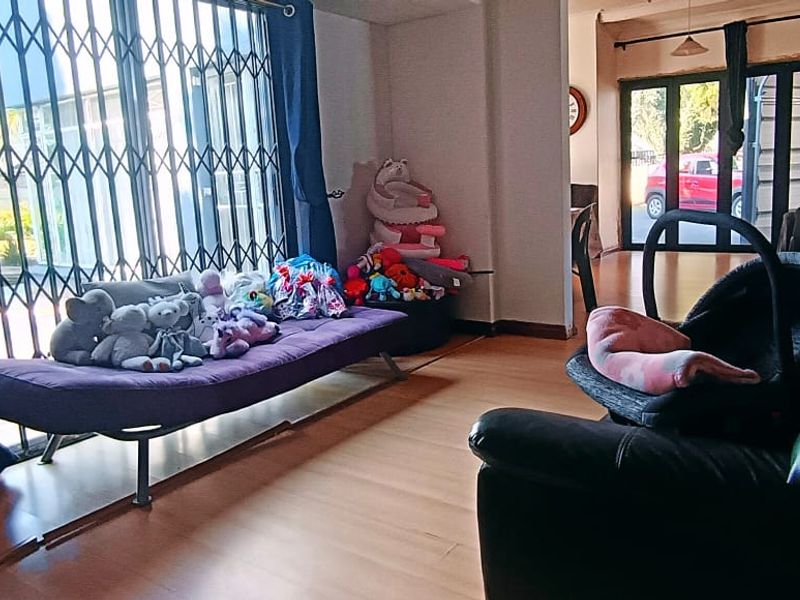 A living room area featuring laminate flooring and a security gate over the sliding door, providing access to the exterior.