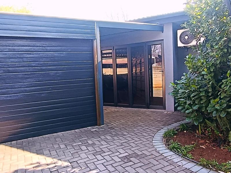 Front exterior view featuring a modern dark garage door, paved driveway, and glass sliding door entrance with an external air conditioning unit.