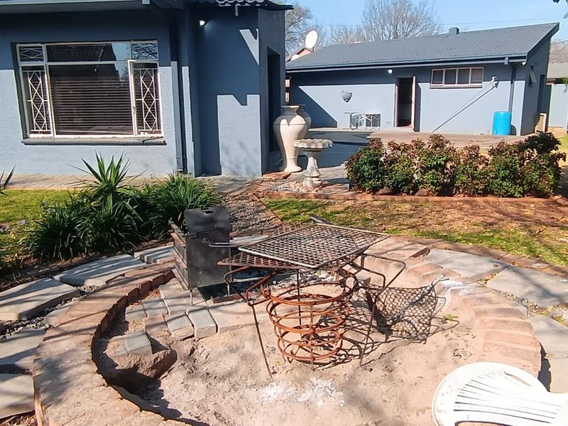 Rear garden area featuring a circular brick-paved fire pit, concrete patio space, and views of the main house and secondary structure.