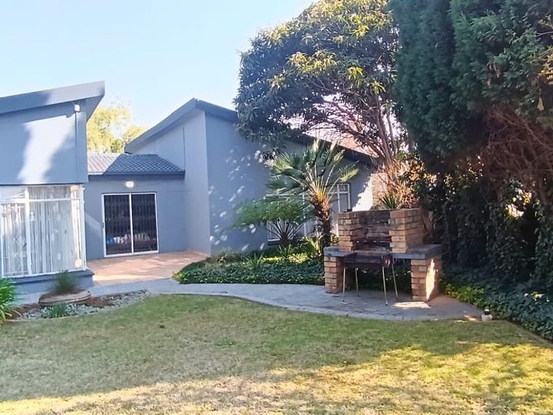Rear view of the house featuring a paved patio area, a brick built-in braai, and a well-maintained garden.