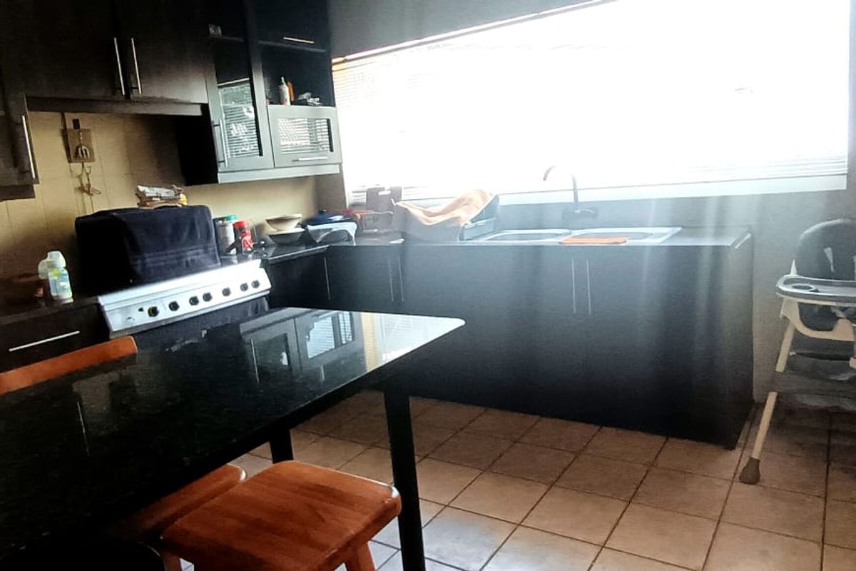 A functional kitchen featuring dark cabinetry, granite countertops, a built-in stove, and tiled flooring with ample natural light from the window.