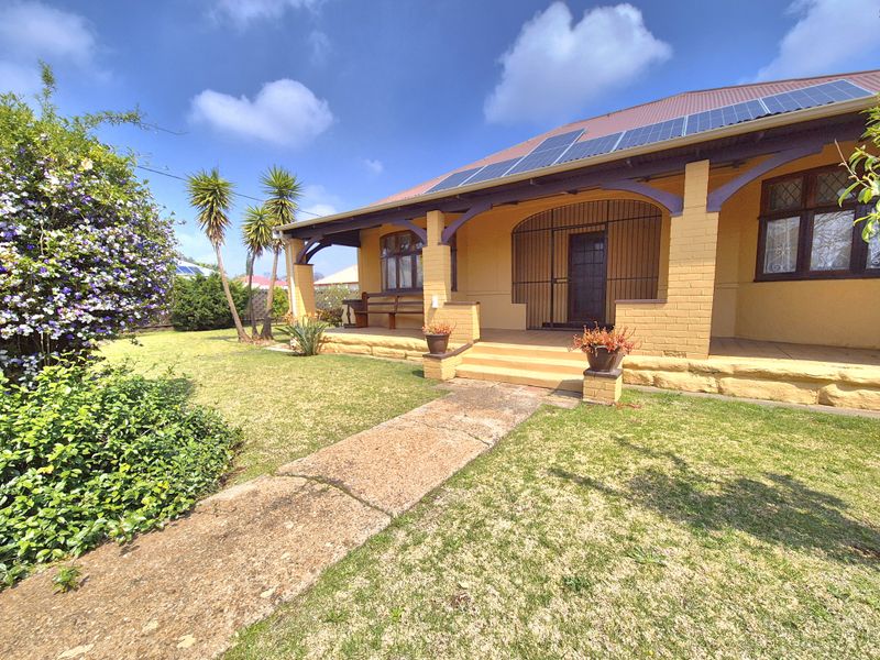 Front elevation of a character home featuring a covered veranda, stone foundation, leaded glass windows, and roof-mounted solar panels set within a landscaped garden.