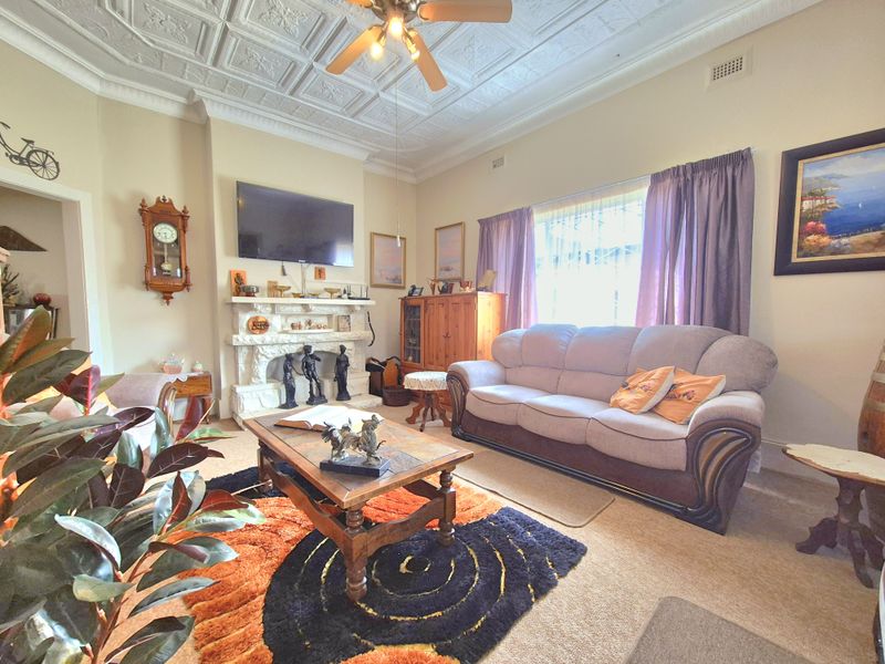A traditional living room featuring a decorative pressed metal ceiling, ornate fireplace mantel, and ceiling fan, offering a classic architectural aesthetic.