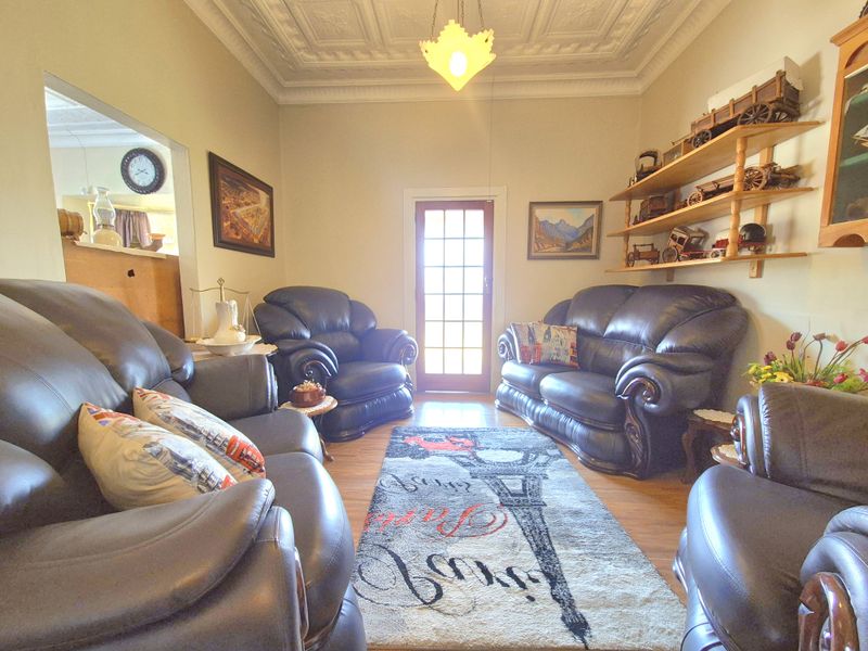 A living room featuring a decorative pressed metal ceiling, timber flooring, and a glass-paneled door providing natural light.