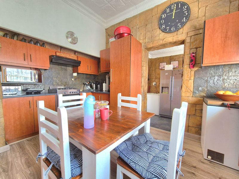 A rustic-style kitchen featuring wooden cabinetry, stone-clad feature walls, a gas stove with extractor, and a pressed ceiling, offering a warm, traditional aesthetic.