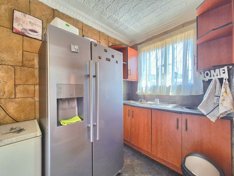 A compact kitchen featuring wood-finish cabinetry, stone-clad walls, a pressed metal ceiling, and a stainless steel sink with a tiled backsplash.