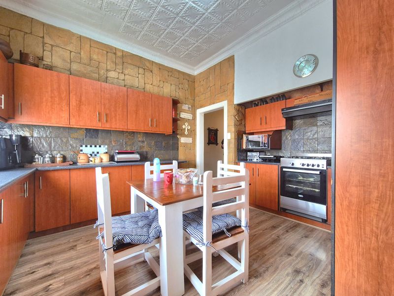 A kitchen featuring warm-toned laminate cabinetry, stone-look wall accents, a pressed metal ceiling, and a freestanding oven with an integrated extractor fan.