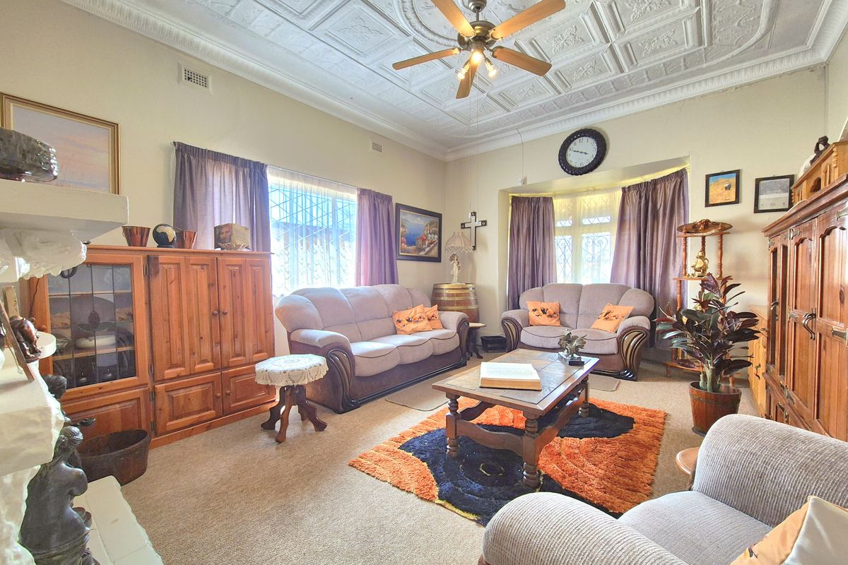 A spacious living room featuring a classic pressed metal ceiling, a ceiling fan, and a bay window with security bars.