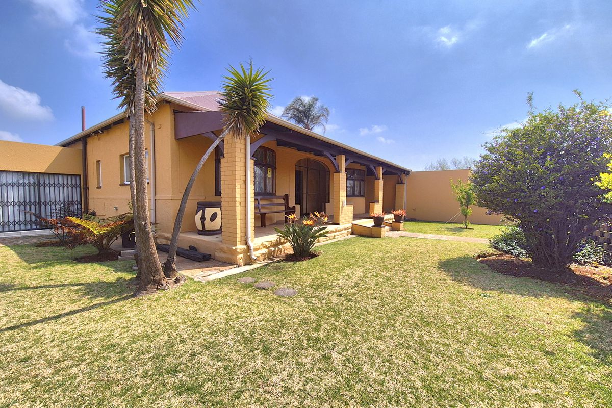 A well-maintained rear exterior view featuring a covered patio with brick pillars, overlooking a neat garden area.