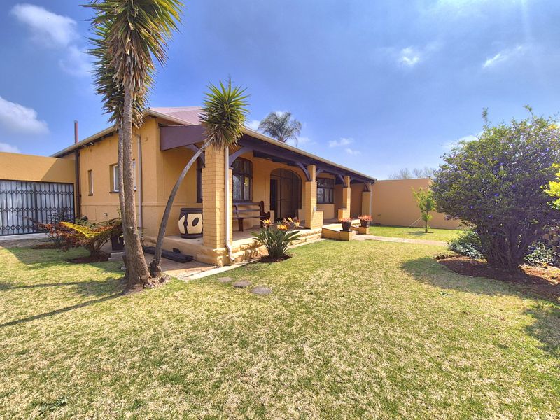 A well-maintained rear exterior view featuring a covered patio with brick pillars, overlooking a neat garden area.