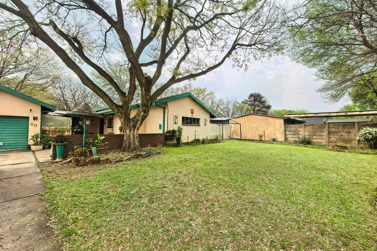 A spacious rear garden featuring a large lawn, mature trees, and a detached garage with a concrete driveway.