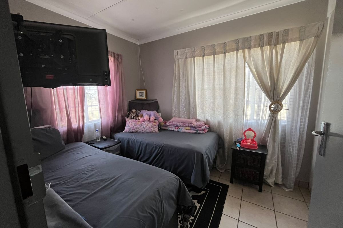 A functional bedroom featuring tiled flooring, neutral wall tones, and a wall-mounted television bracket, offering a practical space for rest.