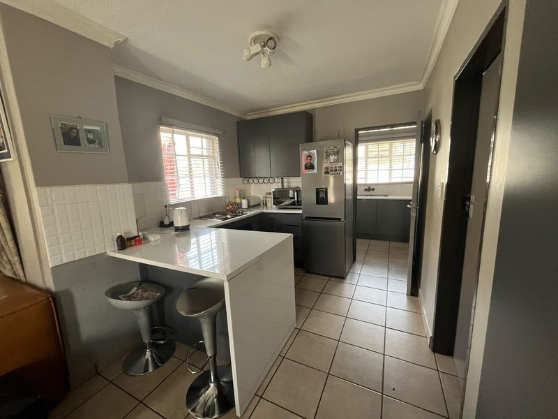 A functional kitchen featuring dark cabinetry, a white stone breakfast bar, tiled flooring, and an adjoining scullery area with additional storage.