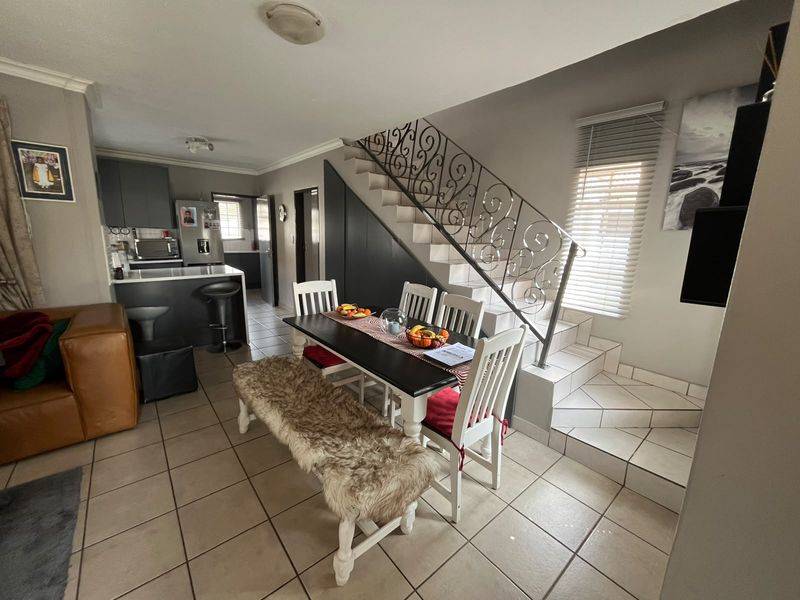 Open-plan living and dining area featuring tiled floors, a modern kitchen with island, and a decorative wrought iron staircase with under-stair storage.