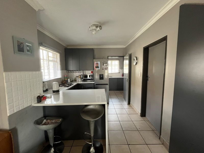 A functional kitchen featuring dark cabinetry, a breakfast bar, tiled flooring, and an adjoining scullery area with additional storage and workspace.