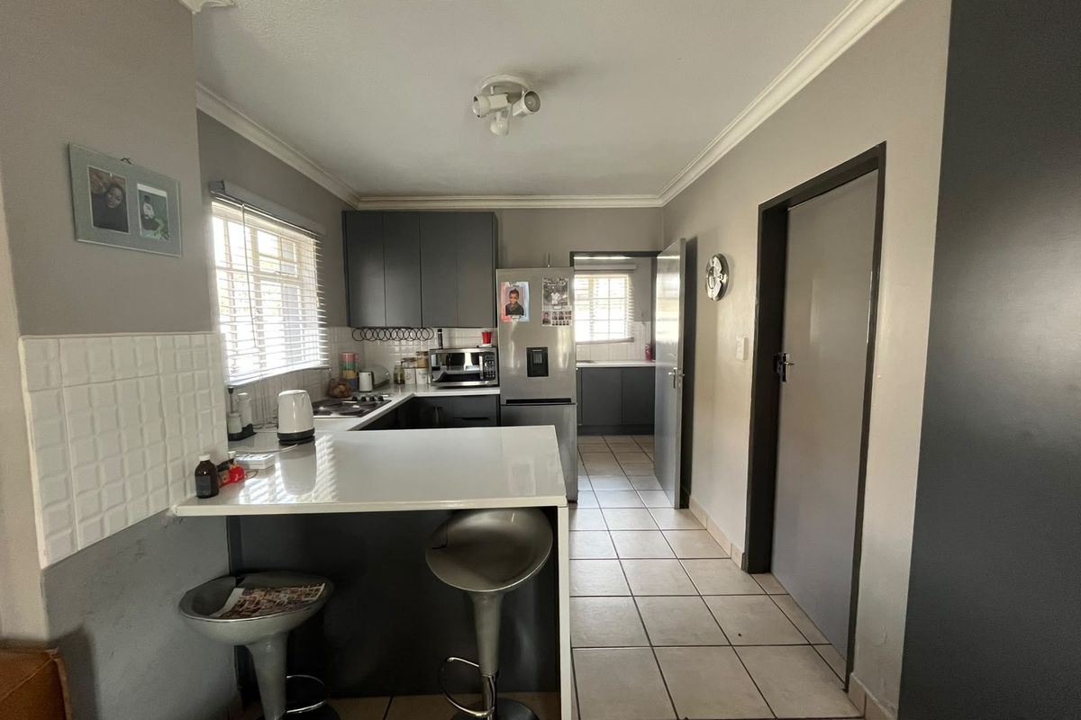 A functional kitchen featuring dark cabinetry, a breakfast bar, tiled flooring, and an adjoining scullery area with additional storage and workspace.