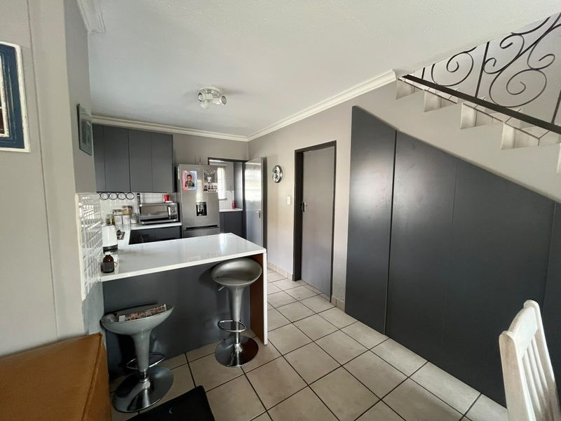 Modern kitchen featuring dark grey cabinetry, a breakfast bar, tiled flooring, and integrated under-stair storage space.