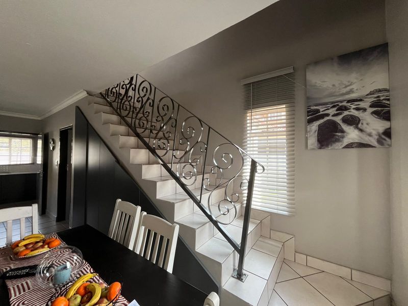 A well-maintained hallway featuring a tiled staircase with decorative wrought iron balustrades and integrated under-stair storage cabinetry.