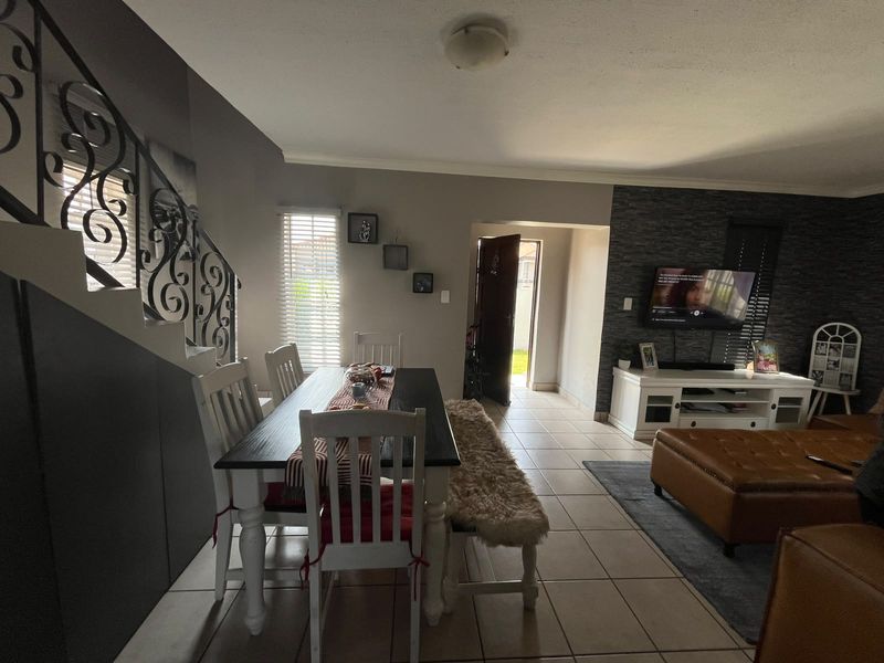 Open plan living and dining area featuring tiled floors, a wrought iron staircase railing, and a textured feature wall.