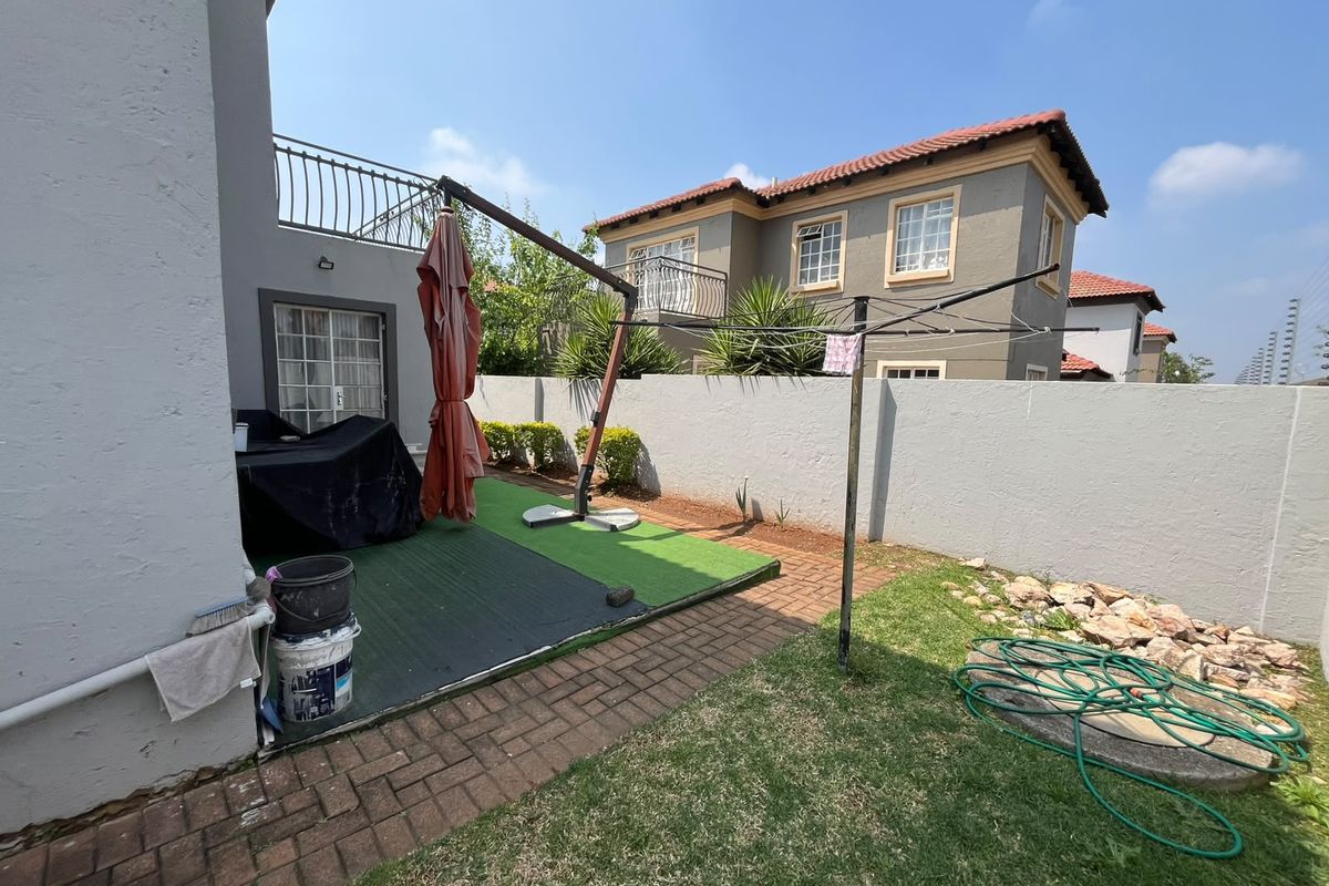 Rear garden area featuring a paved walkway, artificial grass section, and a boundary wall with access to the upper balcony.