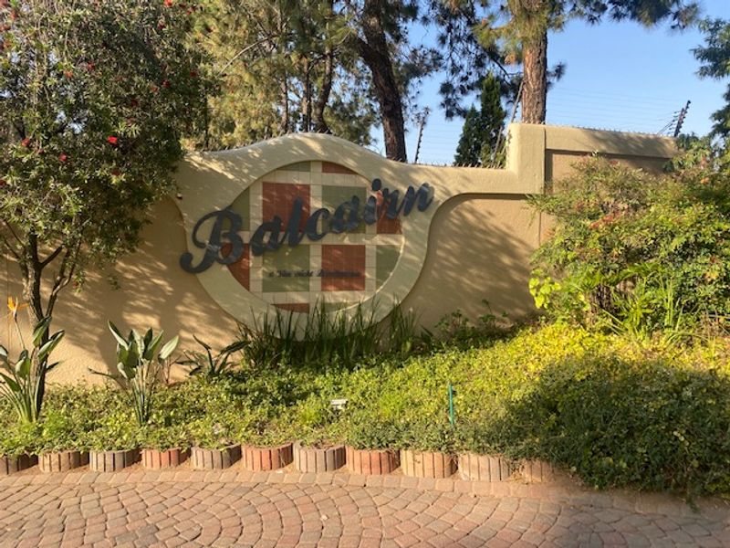 The entrance signage and boundary wall of the Balcairn residential complex, featuring established landscaping and paved driveway access.