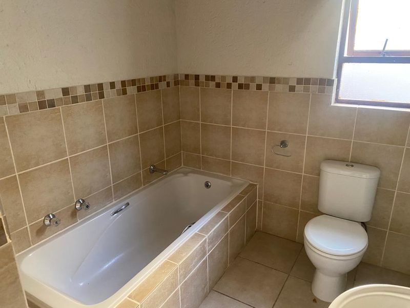 A functional bathroom featuring a built-in bathtub, ceramic wall and floor tiling, and a standard toilet suite.