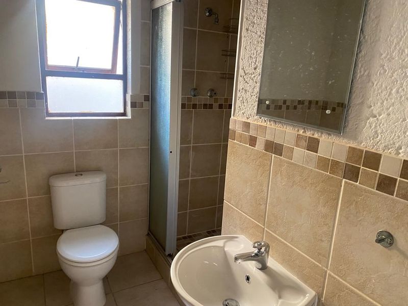 A functional bathroom featuring a shower enclosure, pedestal basin, and toilet with neutral wall tiling. The space would benefit from cosmetic updates.