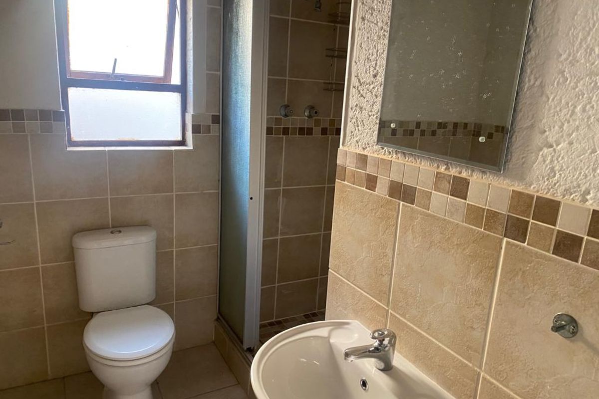 A functional bathroom featuring a shower enclosure, pedestal basin, and toilet with neutral wall tiling. The space would benefit from cosmetic updates.