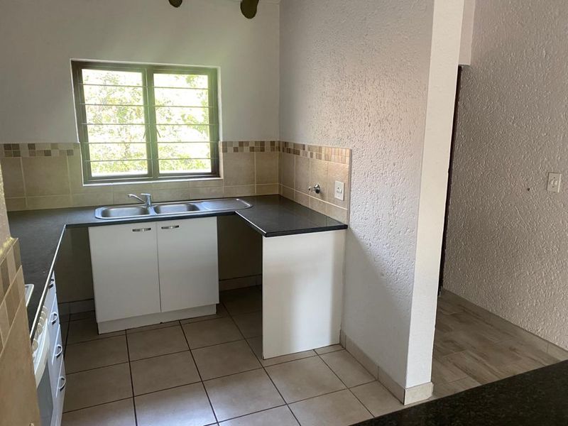 A functional kitchen featuring a double bowl sink, laminate countertops, tiled backsplash, and ceramic floor tiles, offering a clean and practical workspace.