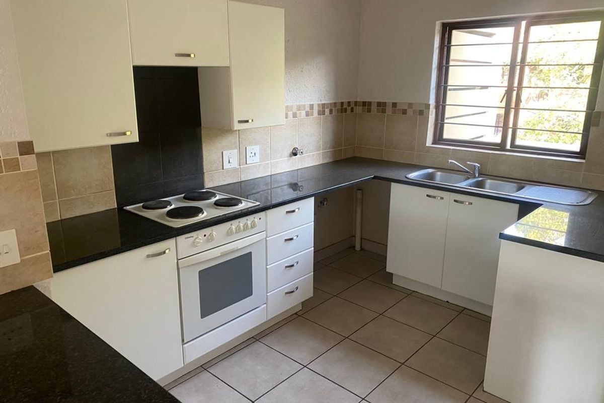 A functional kitchen featuring white cabinetry, dark granite countertops, an electric hob, built-in oven, and a double sink with tiled flooring and splashbacks.