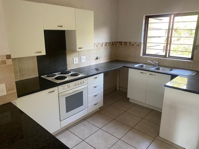 A functional kitchen featuring white cabinetry, dark granite countertops, an electric hob, built-in oven, and a double sink with tiled flooring and splashbacks.