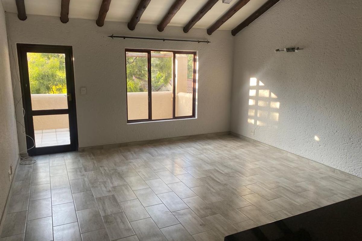 Spacious living area featuring exposed timber ceiling beams, modern tiled flooring, and direct access to an outdoor balcony through a glass panel door.