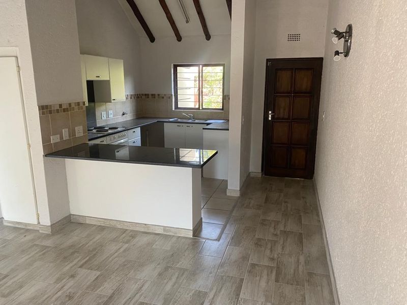 Open-plan kitchen featuring granite countertops, built-in cabinetry, and electric hob, set under a high ceiling with exposed timber beams and tiled flooring.