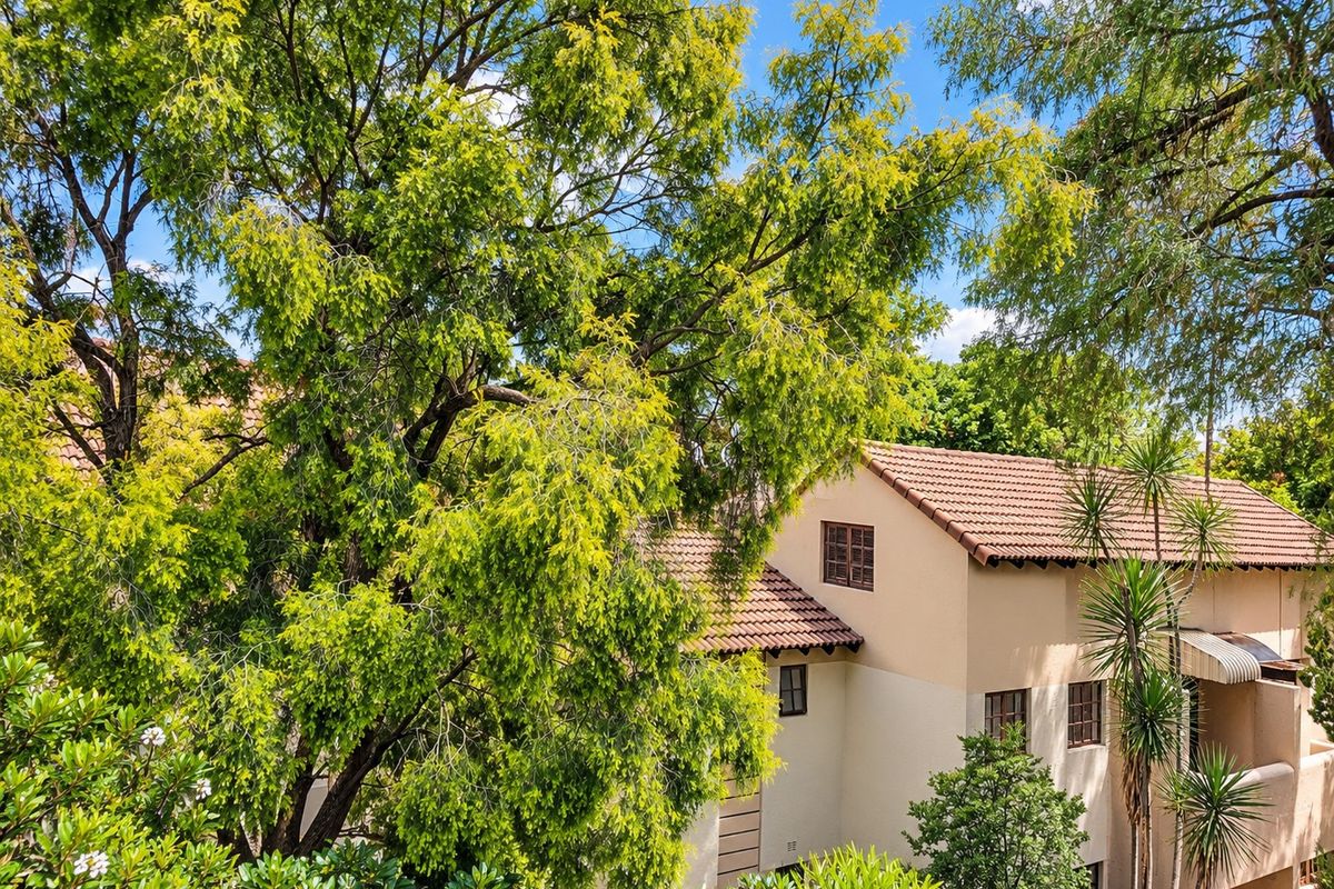 An elevated view of the townhouse exterior featuring a tiled roof, stucco facade, and mature surrounding trees.