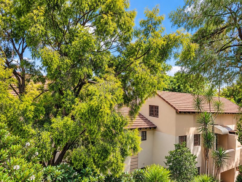 An elevated view of the townhouse exterior featuring a tiled roof, stucco facade, and mature surrounding trees.