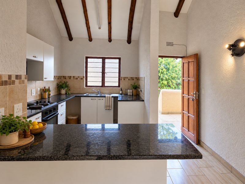 A well-lit kitchen featuring granite countertops, built-in oven, gas hob, and exposed timber ceiling beams, with direct access to an outdoor patio area.