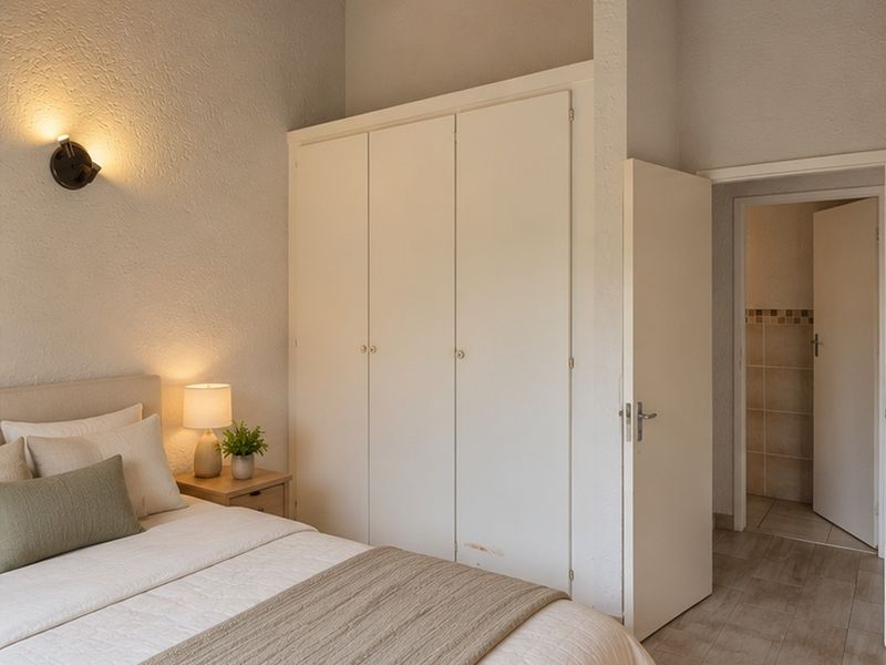 A bedroom featuring built-in wardrobes, textured walls, and tiled flooring, with an adjacent bathroom visible through the doorway.
