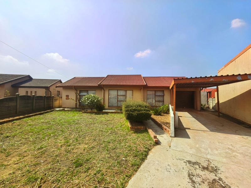 Front view of a single-story house featuring a tiled roof, attached carport, concrete driveway, and a fenced front garden area.